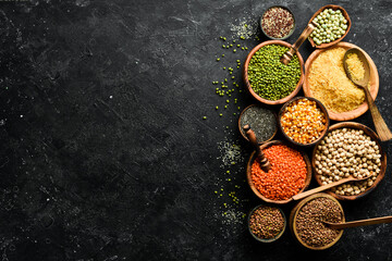 Legumes, a set consisting of different types of beans, lentils and peas, rice and buckwheat on a black background, top view. The concept of healthy and nutritious food
