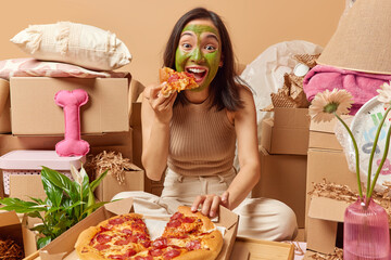 Happy brunette woman eats appetizing pizza feels hungry after relocation to new apartment applies...