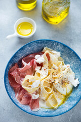 Creamy pappardelle pasta served with prosciutto, ricotta and poached egg, vertical shot on a light-blue stone background