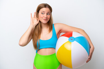 Young woman holding beach ball in holidays isolated on white background listening to something by...