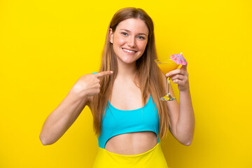 Young caucasian woman holding a cocktail isolated on yellow background with surprise facial expression