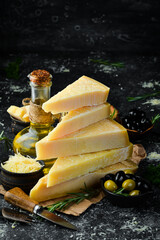 Hard cheese with olives and cheese knife on black stone background. Parmesan. Top view. Free space for your text.