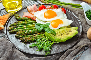 Breakfast. Scrambled eggs, asparagus, bacon and avocado. On a black stone plate.