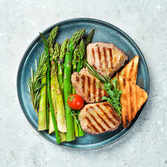 Steak. Veal medallions with asparagus, tomatoes and toast. On a black stone plate.