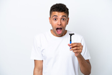 Young Brazilian man shaving his beard isolated on white background with surprise and shocked facial expression