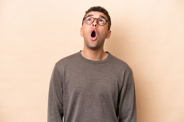 Obraz premium Young Brazilian man isolated on beige background looking up and with surprised expression