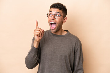 Young Brazilian man isolated on beige background intending to realizes the solution while lifting a finger up