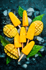 Mango ice cream on a stick. Fresh mango yellow popsicles. On a black stone background. Top view.