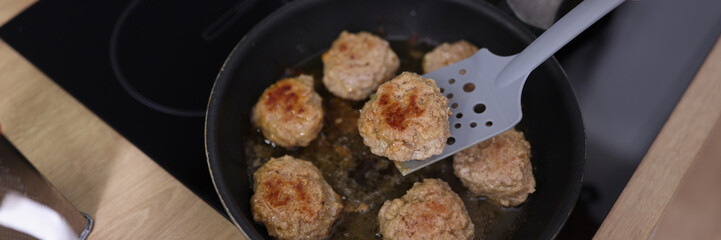 Meat balls beginning to fry in oil in frying pan on kitchen stove