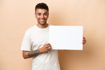 Young Brazilian man isolated on beige background holding an empty placard with happy expression