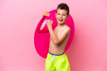 Little caucasian boy holding a inflatable donut isolated on pink background celebrating a victory