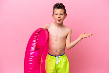 Little caucasian boy holding a inflatable donut isolated on pink background with shocked facial expression