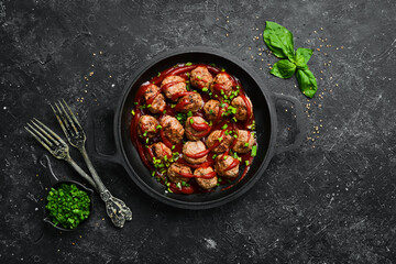 Meatballs in sweet and sour tomato sauce in a frying pan. Top view. On a stone background.