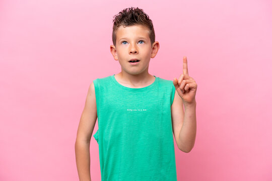 Little caucasian boy isolated on pink background thinking an idea pointing the finger up
