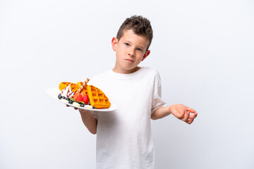 Little caucasian boy holding a waffles isolated on white background making doubts gesture while lifting the shoulders