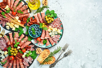 Antipasto snack set: Spanish jamon, Italian prosciutto, cheese set, olives, basil and snacks. Top view. On a gray stone background.