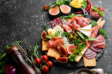 A plate with cheese, salami, prosciutto and snacks on a black stone plate. Antipasto. Top view....