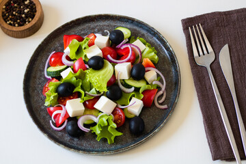 A dish with Greek salad. View from above. Pepper and cutlery are nearby.