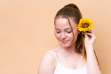 Naklejka premium Young caucasian girl isolated on beige background holding a sunflower. Close up portrait