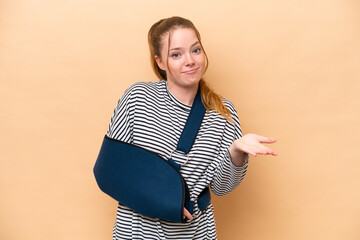 Young caucasian girl with broken arm and wearing a sling isolated on beige background making doubts...