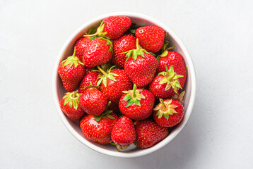 Strawberries in a white bowl close-up on a light background. Top view, close-up