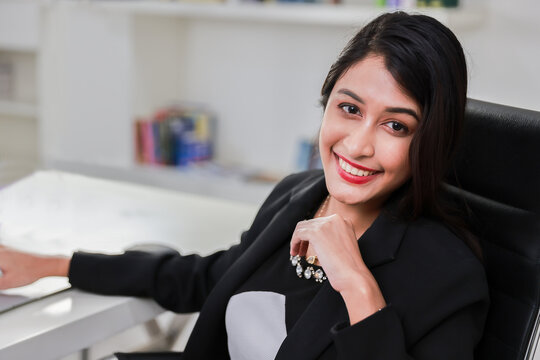 Portrait of cheerful Indian mixed race businesswoman smiling looking at camera working in office with colleague