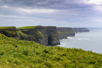 Fototapeta na wymiar Stunning Cliffs of Moher scenery with ocean and green hill covered cliffs alongside the wild Atlantic way in County Clare Ireland