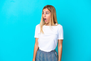 Blonde Uruguayan girl isolated on blue background doing surprise gesture while looking to the side