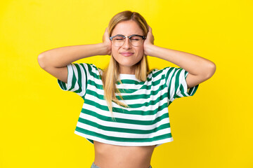 Blonde Uruguayan girl isolated on yellow background frustrated and covering ears