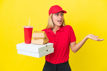 Delivery Uruguayan woman holding fast food isolated on yellow background with surprise expression while looking side