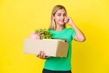 Young Uruguayan girl making a move while picking up a box full of things isolated on yellow...