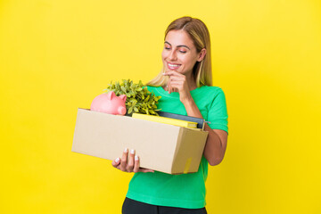 Young Uruguayan girl making a move while picking up a box full of things isolated on yellow...