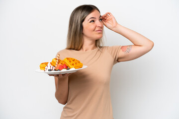 Young Rumanian woman holding waffles isolated on white background having doubts and with confuse face expression