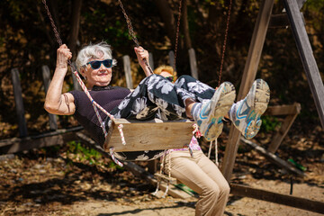 Two elderly women joyfully swinging on a swing and having fan. Happy retirement concept