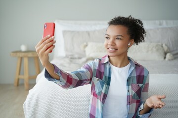 Video phone call. Young african american woman is talking to friend on smartphone in bedroom.