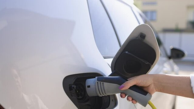 Close up of woman hand holding electric car cable for recharge plug in hybrid electric vehicle at home or charging station. World Environment Day. Save world save life concept