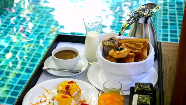 Breakfast served at resort or hotel private villa by swimming pool. Tray with eggs benedict, fresh pastry, orange juice and coffee cup on poolside table. Summer travel, holidays, vacations concept.