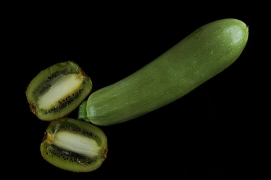 2 two halves of Kiwi fruits with seeds and zucchini in the shape of a penis isolated on black background.