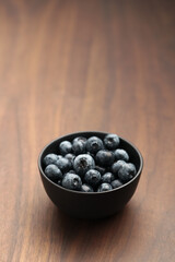 Big organic blueberries in a black bowl on walnut table