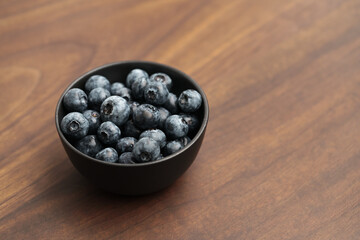 Big organic blueberries in a black bowl on walnut table