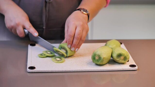 A woman cuts kiwi into slices with a knife