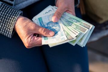 a pensioner holds in her hands banknotes in zloty pensions for payment - obrazy, fototapety, plakaty