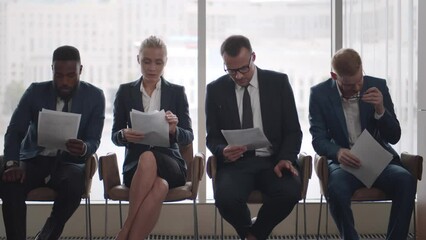Diverse applicants waiting for job interview sitting in line and reading cv. Realtime
