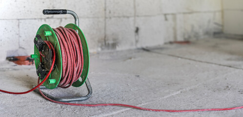 Red and green power cord extension lead drum on construction site ground, closeup detail with empty space for text right side