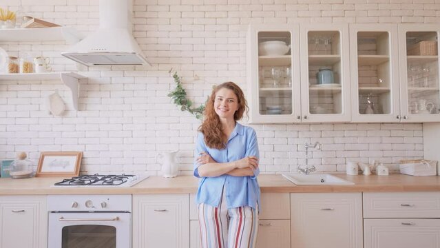 pleased and contented woman posing in the kitchen lady with beautiful curly hair dressed casual shirt looking camera happy owner in apartment