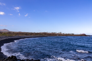 Scenic view on black stone pebble beach Playa Colmenares near Amarilla, Golf del Sur, Tenerife, Canary Islands, Spain, Europe. Vacation resort complex. Waves from Atlantic Ocean. Montana Roja in back