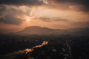 Luang Prabang, Laos - January 29th, 2020 : view from Mount Phousi on the city of Luang Prabang, the Mekong river and the surrounding mountains in the background at sunrise.