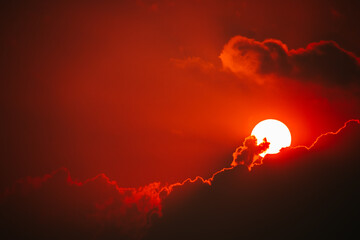 Dramatic fiery red sunset sky with a white sun and dark clouds. Fantastic, magical, fantasy scene. End of the world.