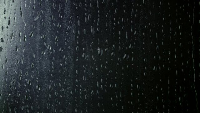 Rain on window. Drops Dripping Down The Glass. Water Drops following down on dark background. 4k video