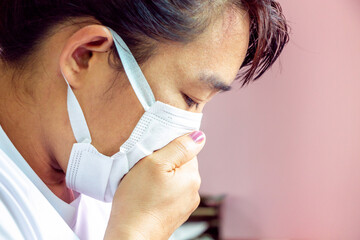 Closeup portrait Asian lady wearing a face mask and putting a hand on her mouth because of cough and illness. Health care concept.